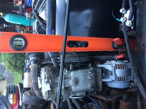 1995 Jeep Wrangler - A close-up view of an engine bay with an orange level tool placed across the top. A silver alternator and a portion of the engine block are…