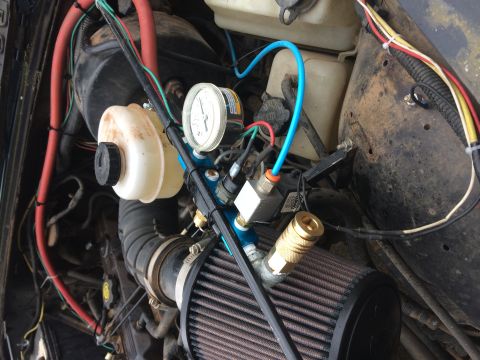 1995 Jeep Wrangler - A close-up view of a modified engine bay, showing a white fluid reservoir, a pressure gauge, and an air intake with a brown filter.