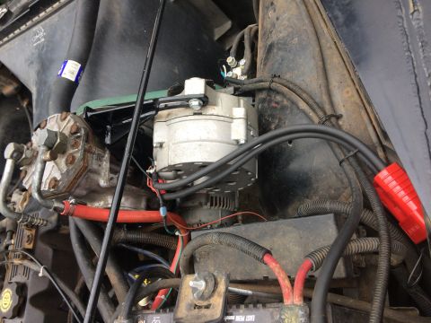 1995 Jeep Wrangler - This is a close-up, angled view of the engine bay of a Jeep YJ, focusing on the alternator and air conditioning compressor. The components…