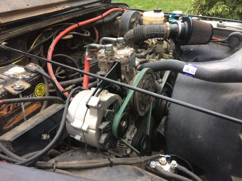 1995 Jeep Wrangler - The engine bay of a Jeep YJ shows the alternator, air intake, and various hoses and wiring. A battery is visible on the left side of the en…