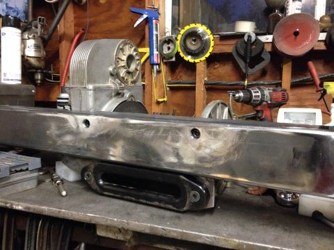 1995 Jeep Wrangler - A metal bumper with a winch mount is shown on a workbench in a garage setting. Various tools and equipment are visible in the background.