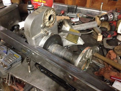 1995 Jeep Wrangler - A workbench is cluttered with tools and mechanical parts, including a winch, a drill, and various metal pieces. The scene appears to be a w…