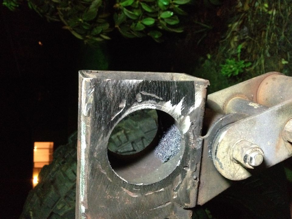 Metal bracket with circular hole and grinding marks, attached to another component.