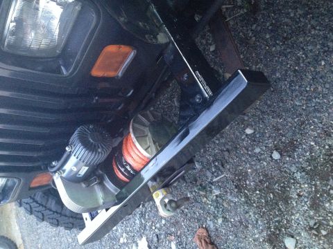 1995 Jeep Wrangler - A close-up, low-angle view of the front bumper and winch assembly of a dark-colored vehicle, possibly a Jeep YJ. The winch features an oran…