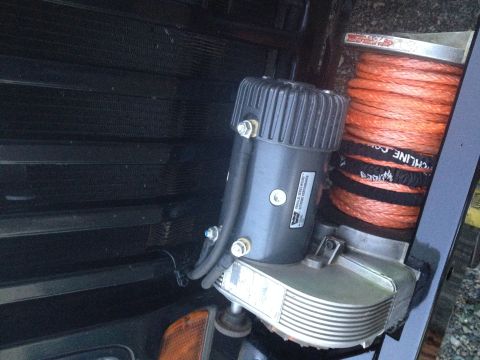 1995 Jeep Wrangler - A close-up view of a winch with an orange synthetic rope, mounted in front of a dark-colored radiator or grille. The winch motor housing ha…
