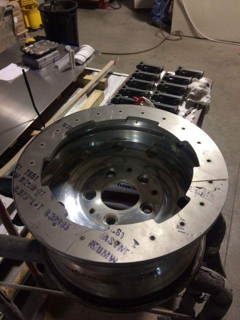 1995 Jeep Wrangler - A close-up view of a large, shiny metal brake rotor with various markings and holes, resting on a metal rim. The rotor is positioned in a w…