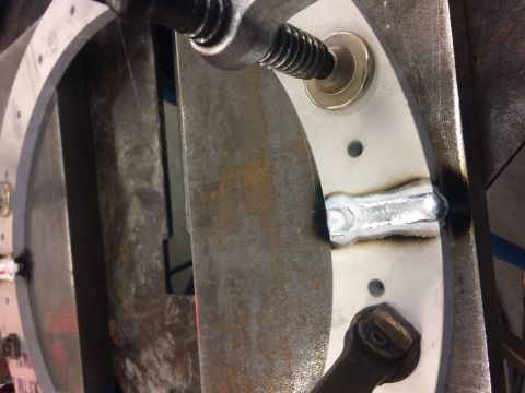 1995 Jeep Wrangler - A close-up view of a metal ring with a freshly welded section. The ring has several pre-drilled holes and is secured by a clamp with a thre…
