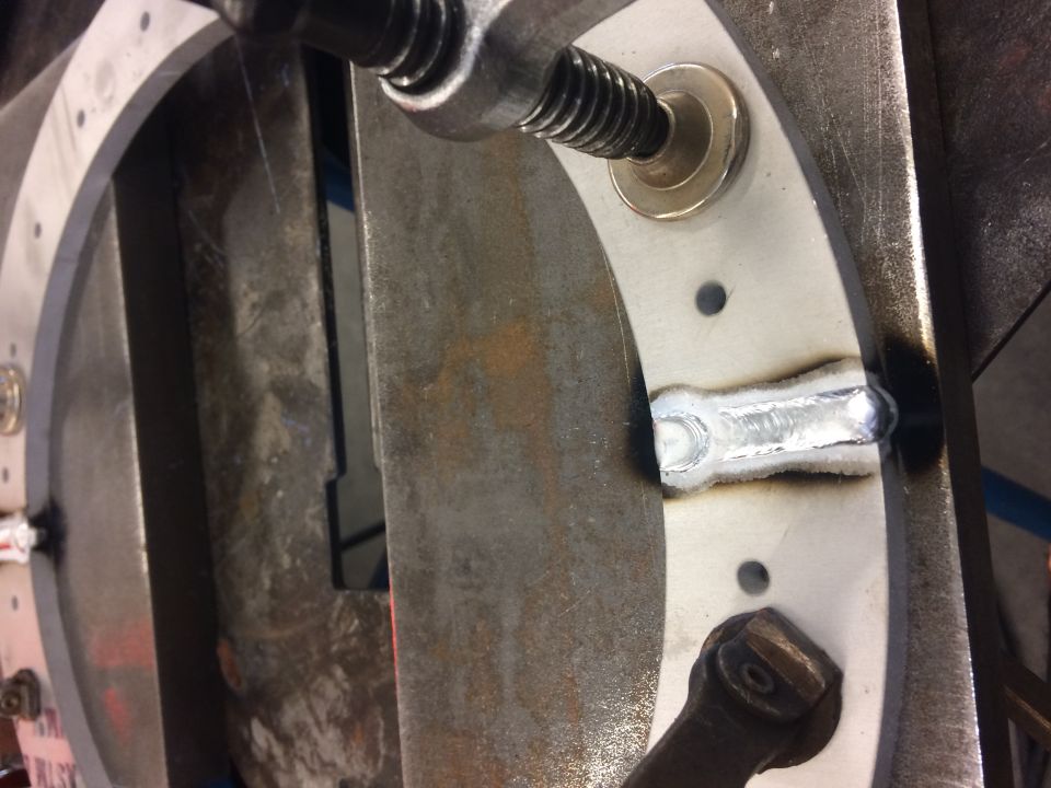 Close-up of a metal ring with a weld, secured by a clamp.