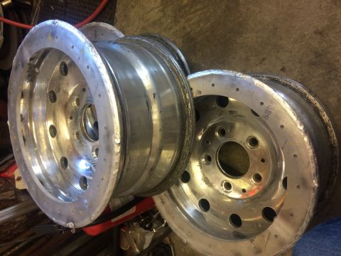 1995 Jeep Wrangler - Two polished aluminum wheels with multiple bolt holes are stacked on a concrete floor. The wheel in the foreground shows a shiny, reflectiv…