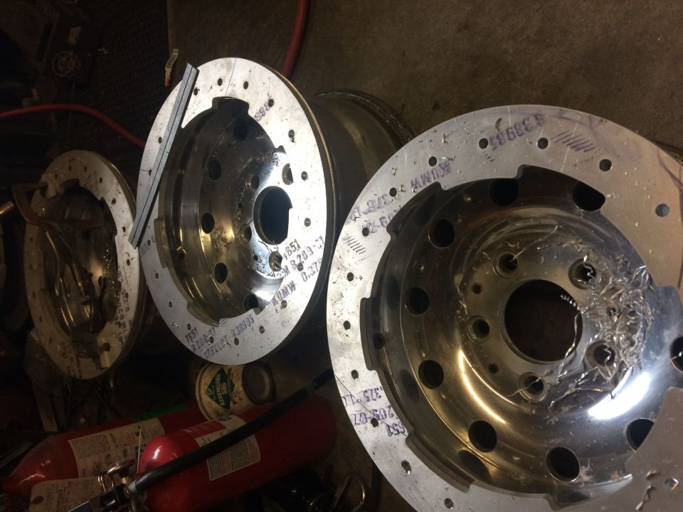 Three custom aluminum wheel hubs, one with machining marks, in a workshop.