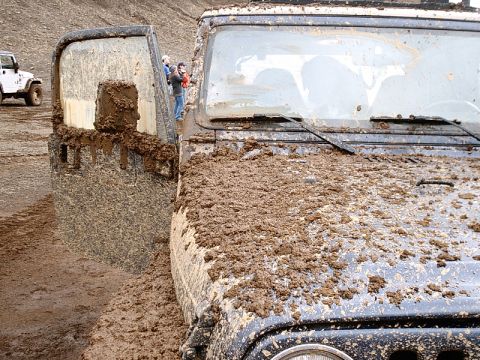 1996 Ford Bronco - Two mud-splattered Jeep Wranglers are stuck in the mud, one with its door ajar.