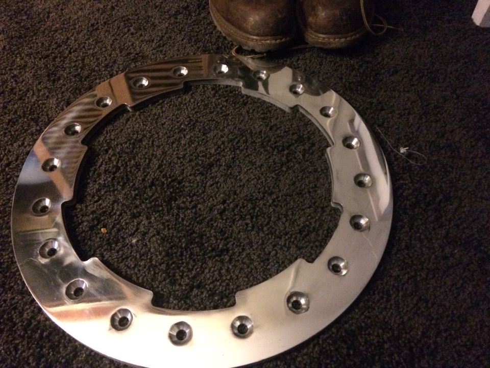 Polished metal ring with bolt holes on carpet next to brown work boots.