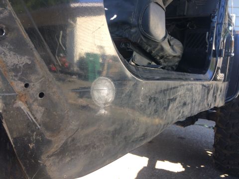1995 Jeep Wrangler - A close-up view of the lower body panel of a black Jeep YJ, showing rust and a circular patch repair on the exterior. The interior door sil…