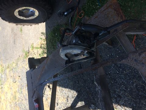 1995 Jeep Wrangler - A circular saw is positioned over a rusty metal structure that appears to be part of a trailer or frame. A large tire and part of a vehicle…