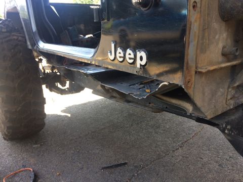 1995 Jeep Wrangler - The lower body panel of a dark colored Jeep YJ is shown with significant damage and rust. The "Jeep" logo is visible on the door panel, and…