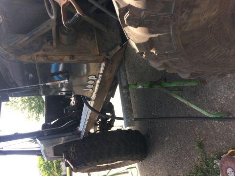 1995 Jeep Wrangler - The underside of a Jeep YJ is shown, with a focus on the frame and suspension components. A green jack is supporting the vehicle near the r…