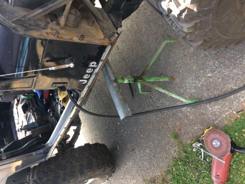 1995 Jeep Wrangler - A black Jeep YJ is shown from a low angle, with its driver's side door open, revealing internal components. A green jack stand and a red an…