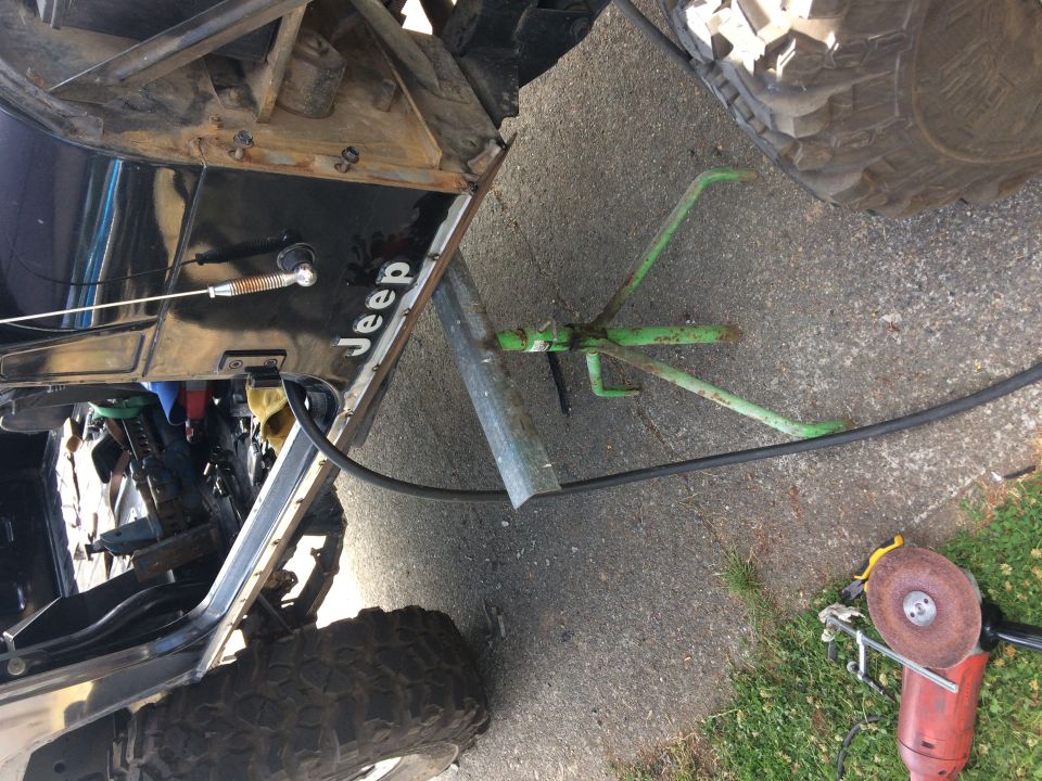Black Jeep YJ with door open, green jack stand, and red angle grinder.