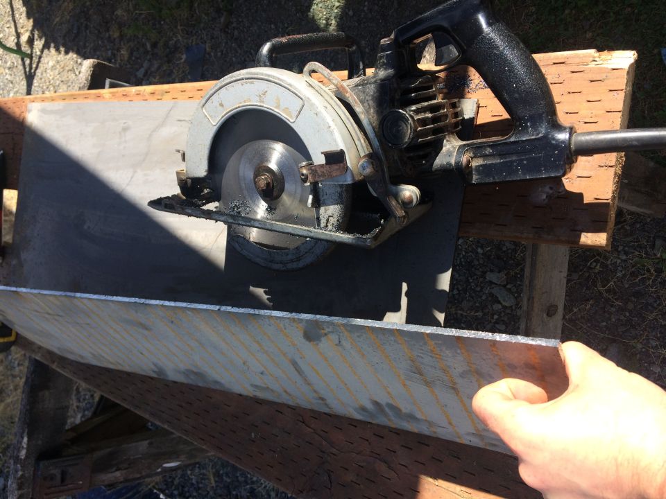 Circular saw cutting metal sheet, hand holding edge.