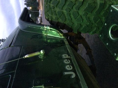 1995 Jeep Wrangler - A close-up, angled view of the rear passenger side of a dark green Jeep YJ. Visible modifications include a large off-road tire, a custom r…