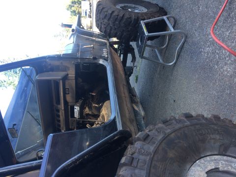 1995 Jeep Wrangler - A black Jeep YJ is parked on asphalt, with its driver's side door open. A large, aggressive off-road tire is visible in the foreground, and…