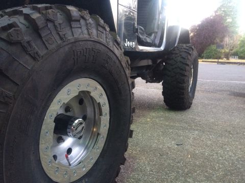1995 Jeep Wrangler - A black Jeep YJ is shown from the side, highlighting its large off-road tires and custom wheels.