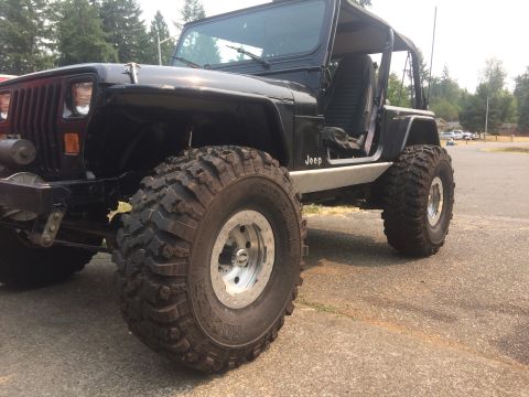 1995 Jeep Wrangler - Modified black Jeep Wrangler with prominent off-road tires and custom rocker panels is parked outdoors.