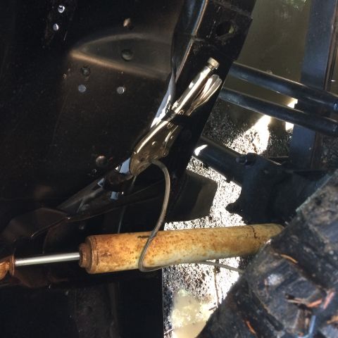 1995 Jeep Wrangler - A close-up view shows a rusty shock absorber secured with vice grips to a black metal frame. The scene appears to be under a vehicle, possi…