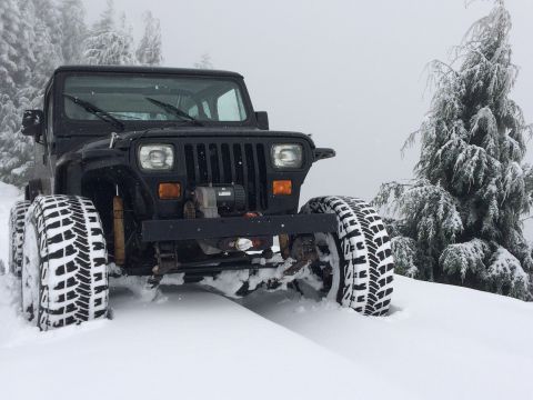 1995 Jeep Wrangler - A black Jeep Wrangler navigates a snowy landscape with its tires deep in the snow.