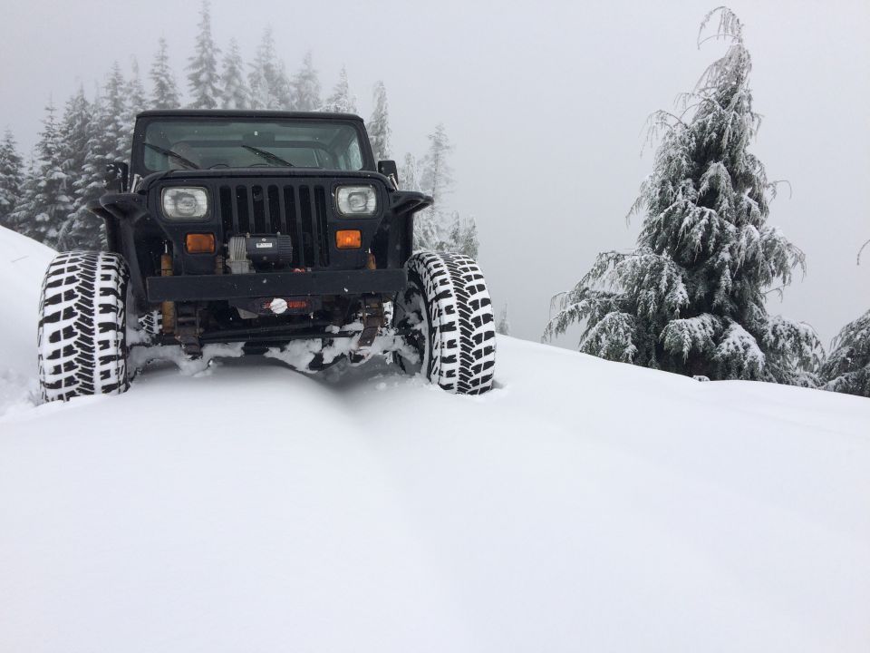 Black 1995 Jeep YJ driving through deep snow on a mountain road