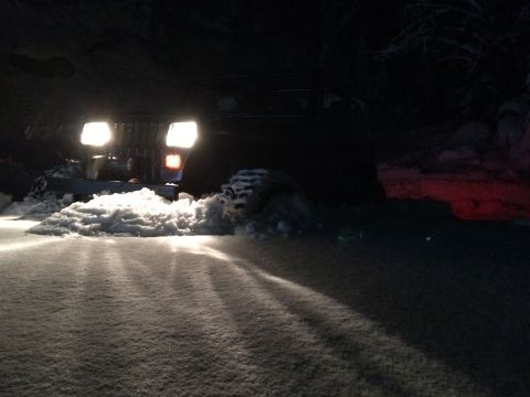 1995 Jeep Wrangler - A Jeep Wrangler navigates a snowy path at night, its headlights cutting through the darkness.