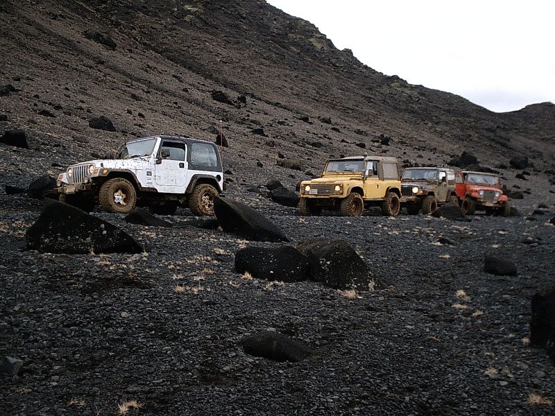 White off-road SUV with three other 4x4s on dark volcanic slope