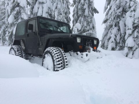 1995 Jeep Wrangler - A black Jeep Wrangler is partially buried in deep snow, with only its front visible.
