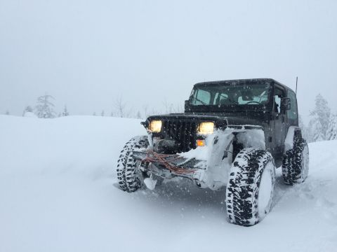 1995 Jeep Wrangler - A Jeep Wrangler navigates through a snowy landscape with its headlights illuminated.