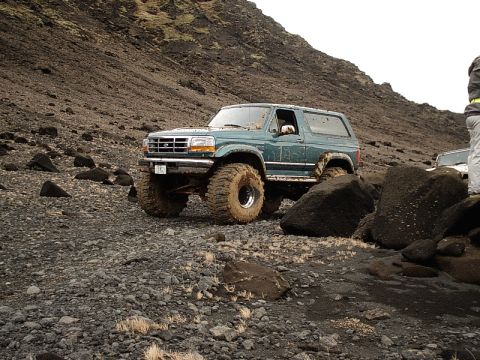 1996 Ford Bronco - A modified 1996 Ford Bronco navigates a challenging off-road terrain with large tires and lifted suspension.