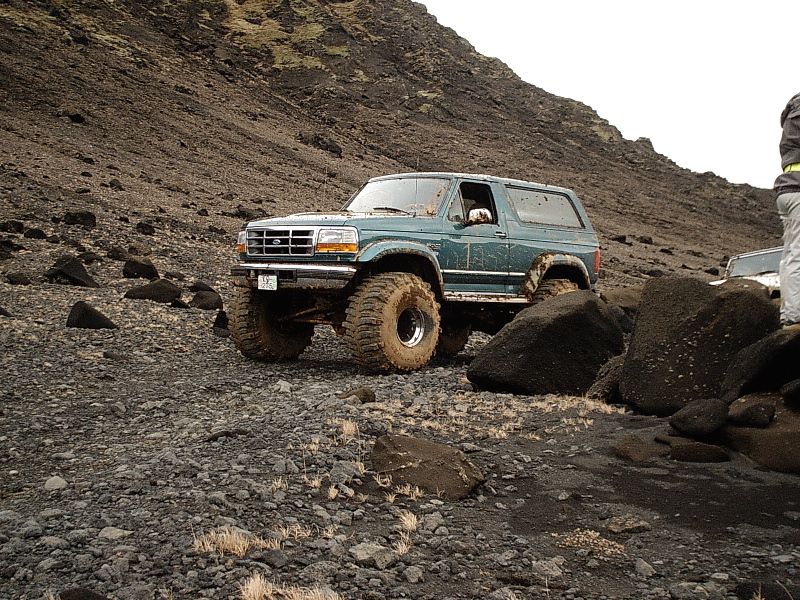 Teal Ford Bronco with lifted suspension and muddy tires on rocky terrain