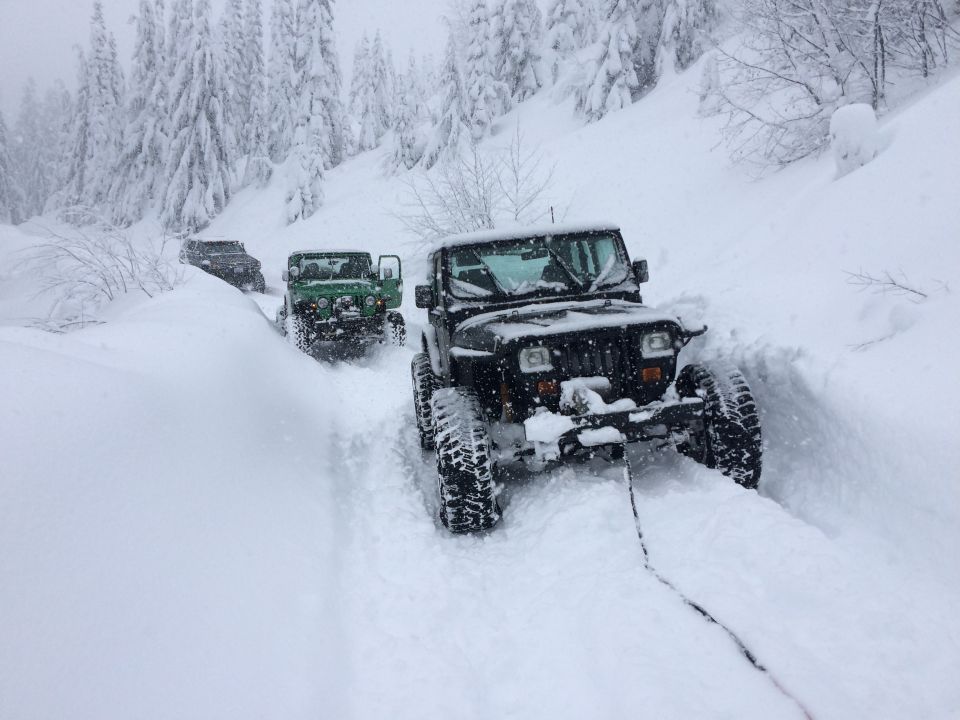 Black Jeep Wrangler being towed in deep snow with other Jeeps behind