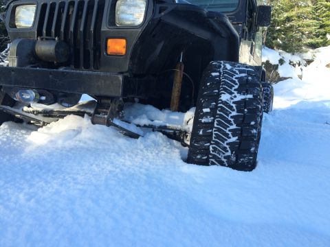 1995 Jeep Wrangler - A Jeep Wrangler is partially buried in snow, with its front tire and bumper visible.