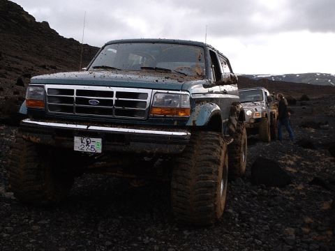 1996 Ford Bronco - A line of off-road vehicles navigates a rocky, barren landscape under an overcast sky.