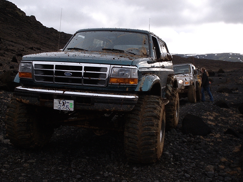 Muddy teal lifted Ford SUV on rocky terrain, front 3/4 view