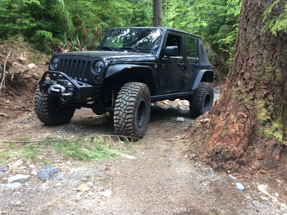 Black Jeep Wrangler with aftermarket bumper and winch on a dirt trail