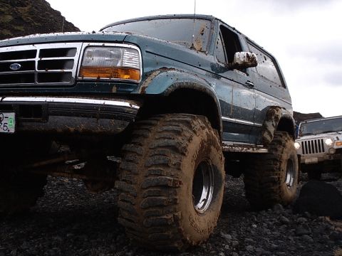 1996 Ford Bronco - This 1996 Ford Bronco, heavily coated in mud, navigates rough terrain alongside another off-road vehicle.