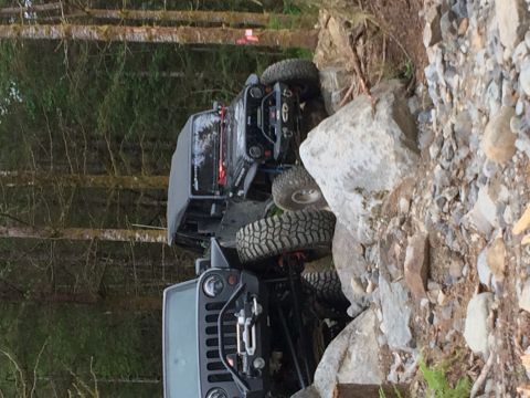 1995 Jeep Wrangler - Two Jeeps tackle a challenging rocky trail, with one vehicle positioned precariously close to a large boulder.