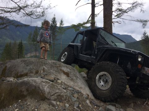 1995 Jeep Wrangler - A young child stands on a boulder while a black Jeep Wrangler navigates a rocky trail.