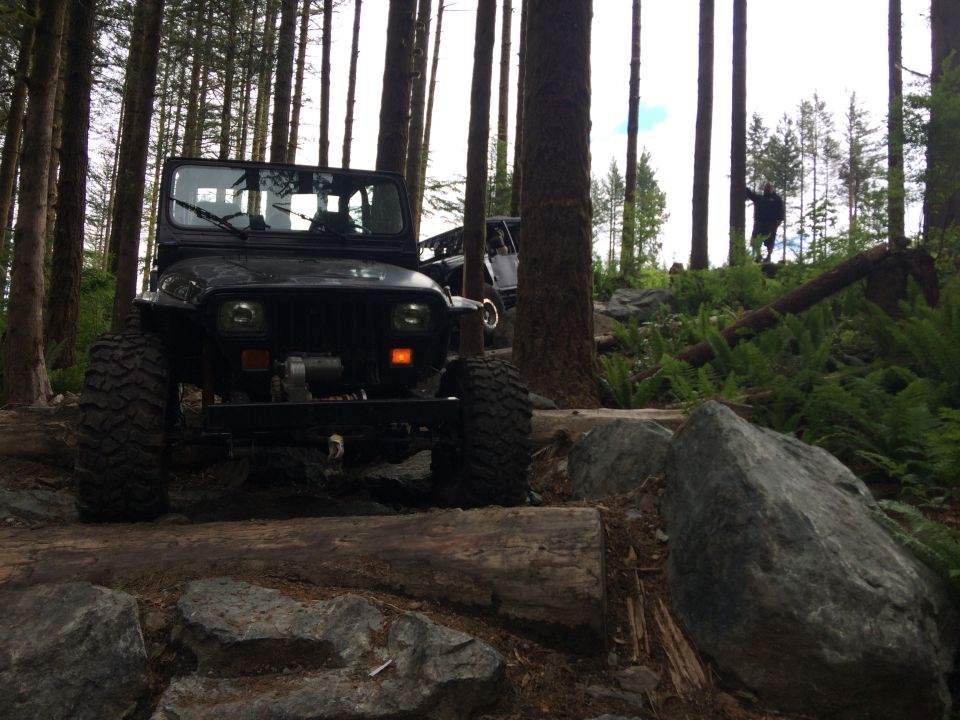 Black Jeep Wrangler on a rocky, wooded trail with large tires and a winch