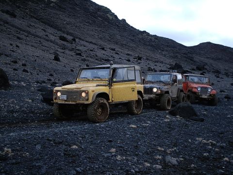 1996 Ford Bronco - A convoy of off-road vehicles, including a yellow Land Rover Defender and two Jeeps, navigates a , rocky terrain under an overcast sky.