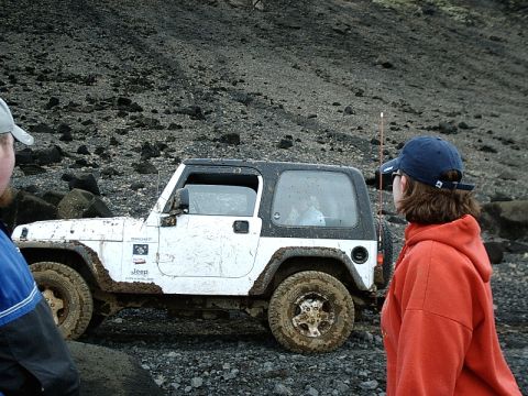 1996 Ford Bronco - Mud-covered Jeep Wrangler parked on a rocky, off-road trail with two observers.