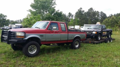 2003 Ford Ranger - A red and silver pickup truck tows a black pickup truck on a trailer. Text is visible on the side of the towed truck.