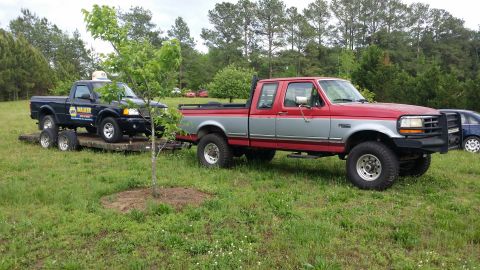 2003 Ford Ranger - A red and silver Ford F-250 tows a black Ford Ranger on a trailer in a grassy area.