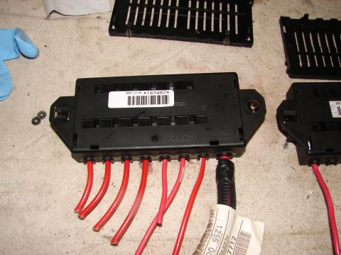 1973 Ford Ranchero - A black fuse box with several red wires is shown, along with two other black plastic components and a blue glove.